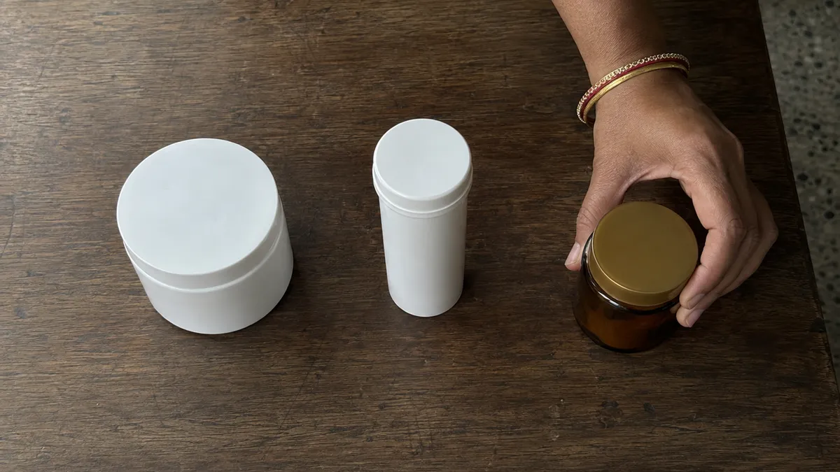 Three unlabelled containers on a wooden table with a hand moving one aside