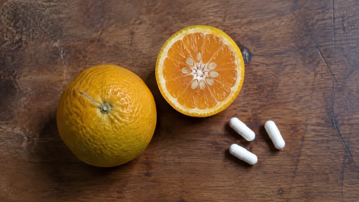 Two bitter oranges, one cut in half, beside three plain white capsules on a wooden table