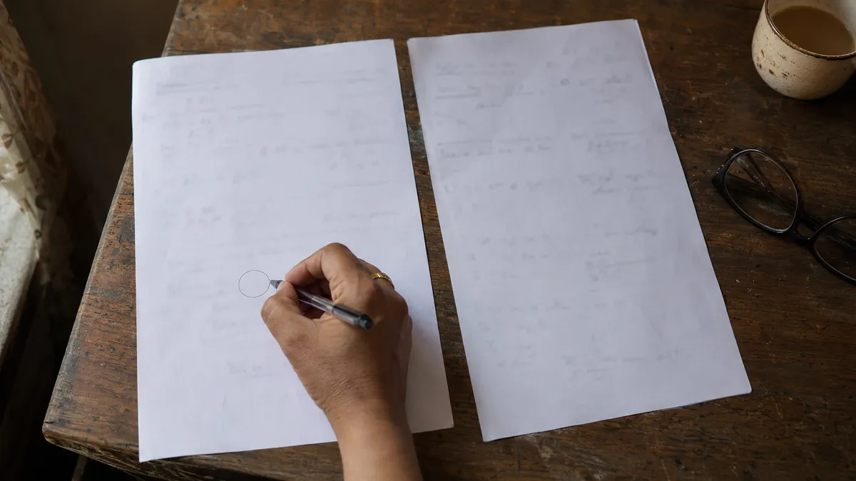 Two sheets of paper side by side on a desk with a hand circling a detail on one of them