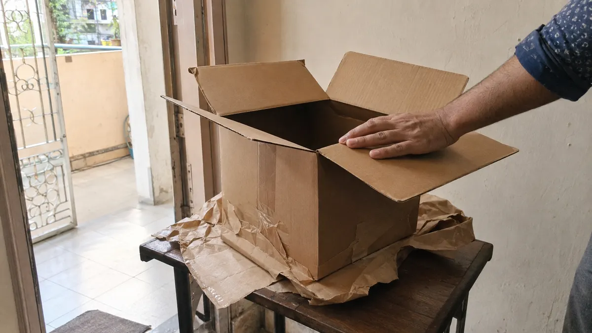 A plain cardboard delivery parcel just opened on a table by a doorway