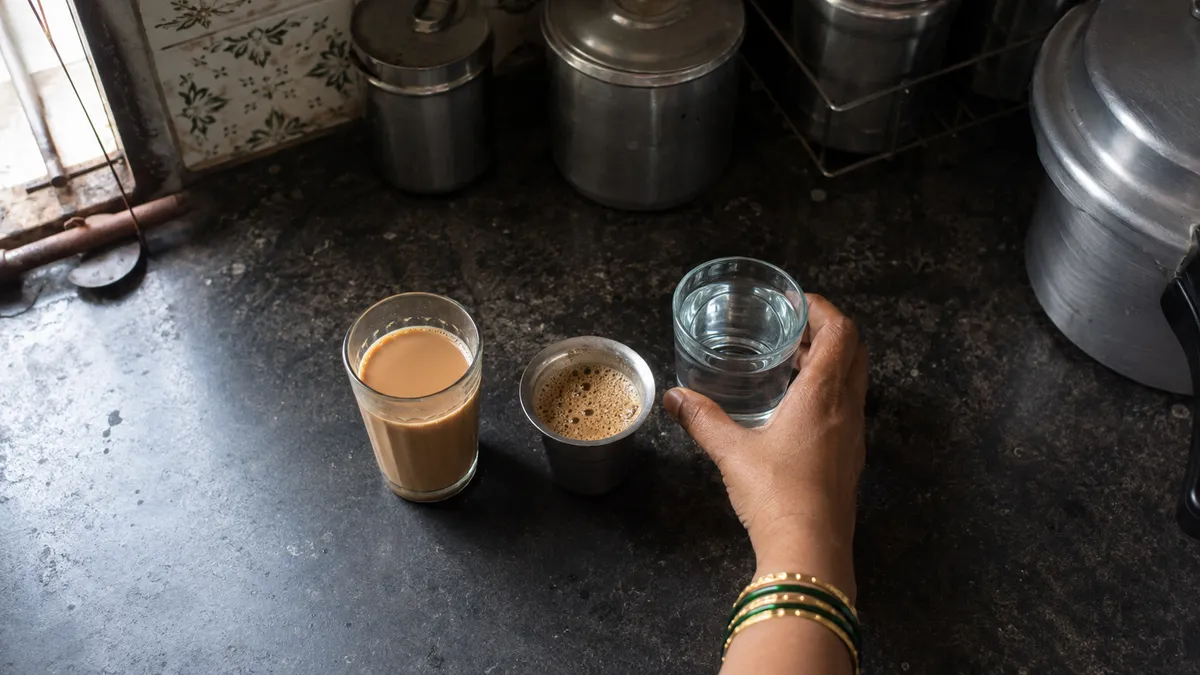 A glass of chai, a steel cup of filter coffee and a glass of water on a kitchen counter