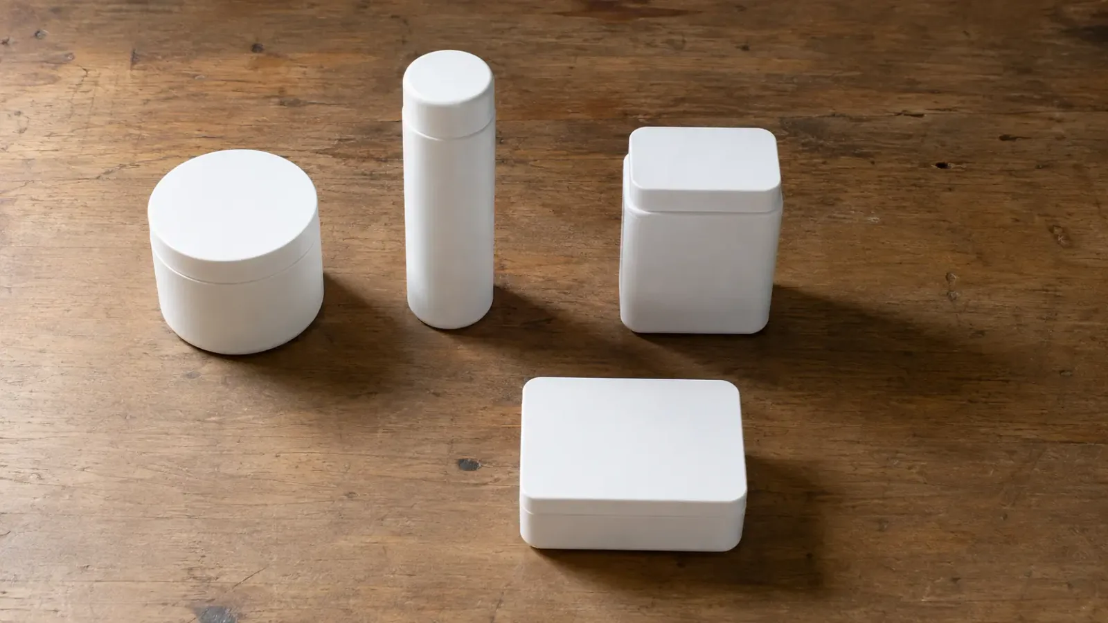 Four unmarked white containers of different shapes on a wooden table, one set apart from the others